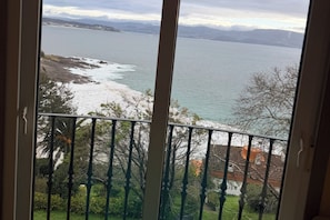 A view from a balcony overlooking a coastal landscape with a body of water, rocky shore, and distant mountains.