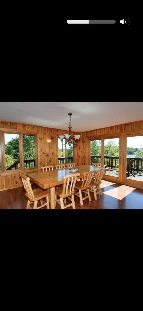 A wooden dining room with a large table and chairs, large windows, and a chandelier.