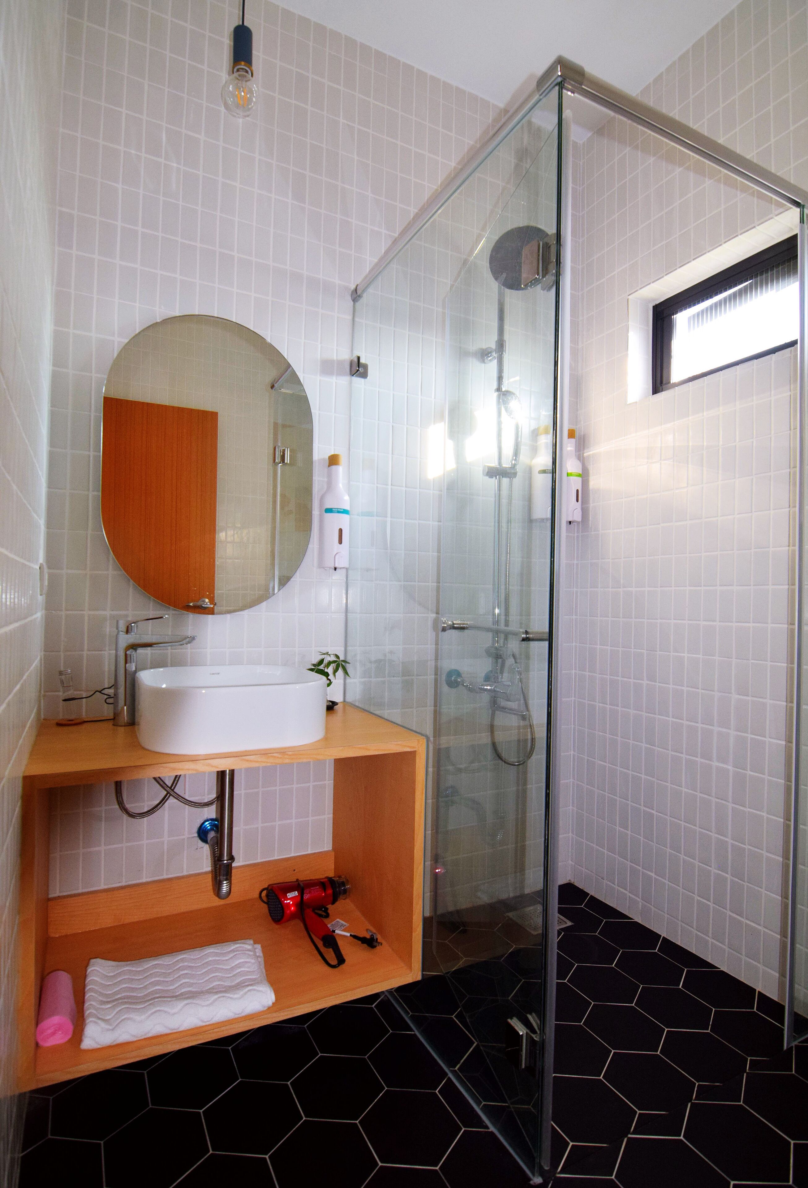 A bathroom with a glass shower enclosure, a round mirror, a sink, and a wooden vanity.