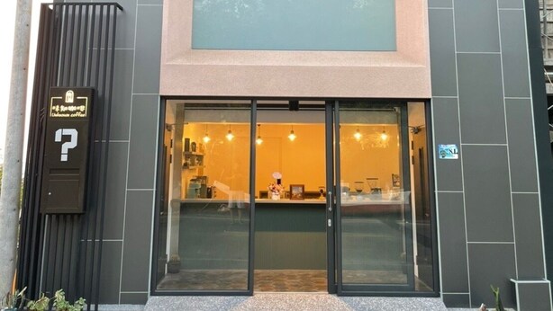 Um edifício moderno com estrutura em dois andares, entrada visível com portas de vidro e uma placa indicando uma cafeteria no interior.