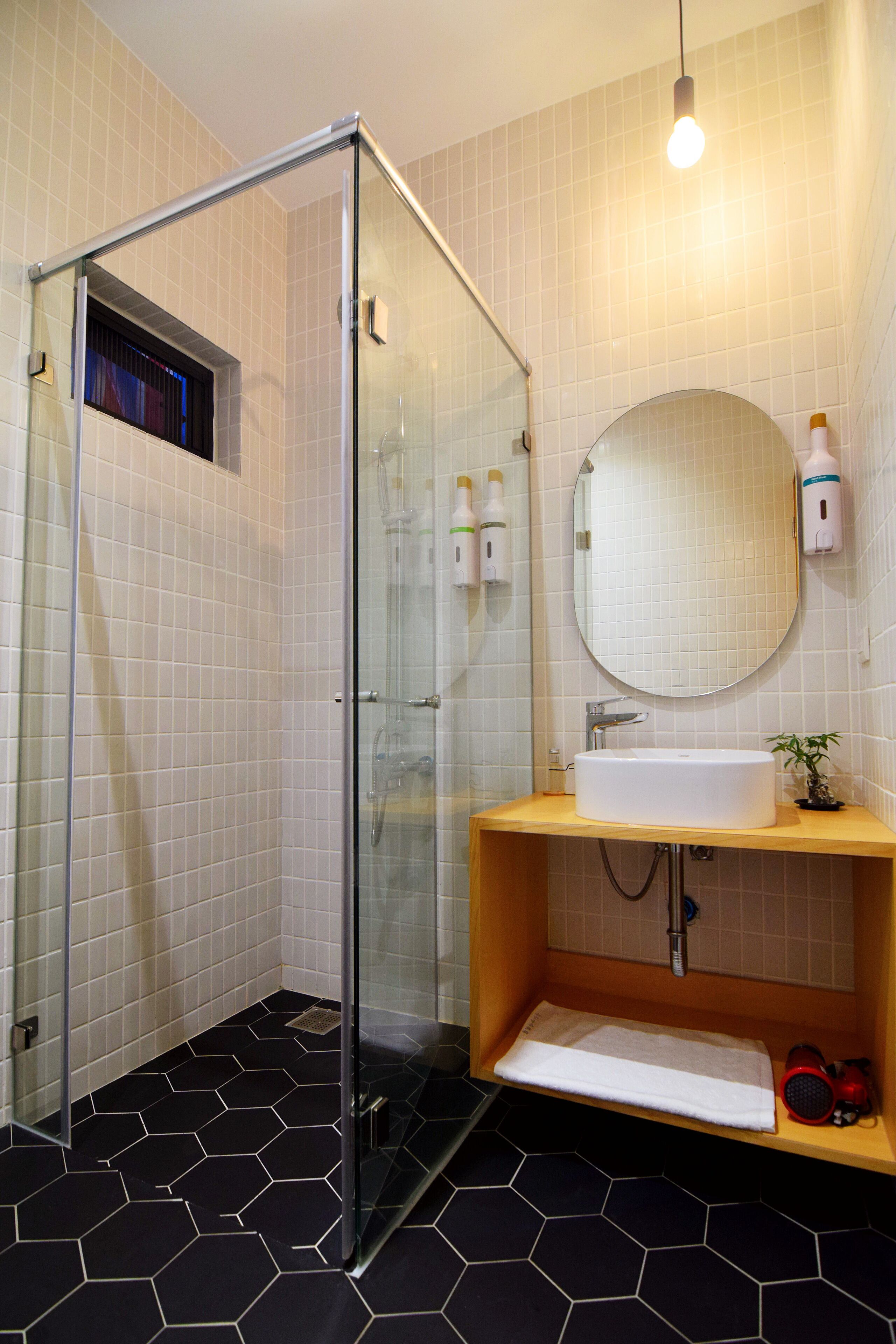 A modern bathroom with a glass shower enclosure, a round mirror, a sink with a wooden vanity, and a black and white tiled floor.