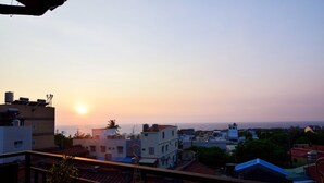 Vista do pôr do sol a partir de uma varanda com vista para uma área residencial, prédios e céu claro.