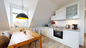 A modern kitchen with white cabinets, a wooden dining table, and a black pendant light.