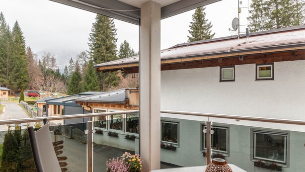 A balcony with a view of a mountain, a wooden deck, and a building with multiple windows.