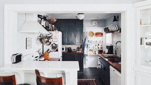 Une cuisine moderne avec des meubles de couleur sombre, un plan de travail blanc et un coin repas comprenant une table blanche et des chaises noires.