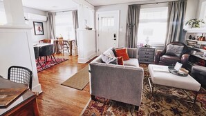 Un salon spacieux avec un canapé gris, une table basse et un coin repas agrémenté d’un tapis rouge.