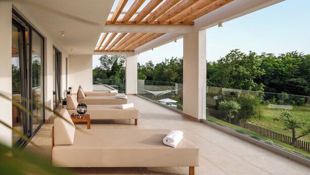 Un moderno espacio lounge al aire libre con dos sofás y una mesa de centro, amplias ventanas con vistas a un jardín ajardinado.