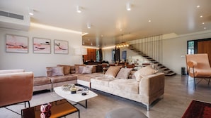 Una sala de estar moderna con un amplio sofá en forma de L, una mesa de centro y una escalera que conduce a un nivel superior.