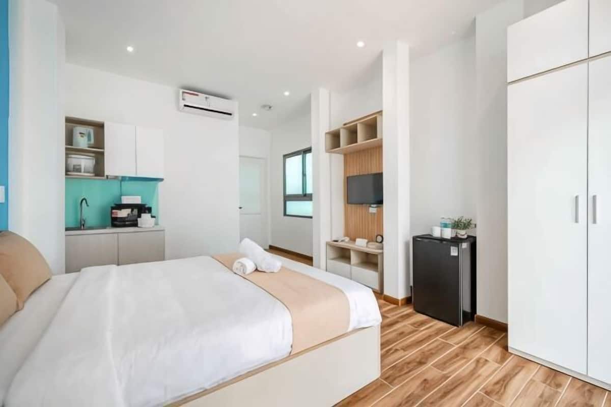 A modern hotel room with a bed, kitchenette, and wardrobe.
