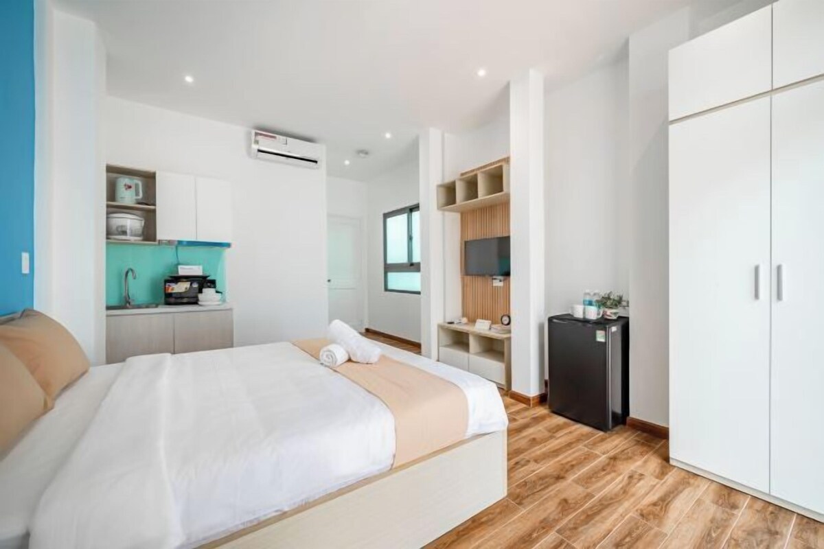 A modern hotel room with a bed, a kitchenette, a TV, and a wardrobe.
