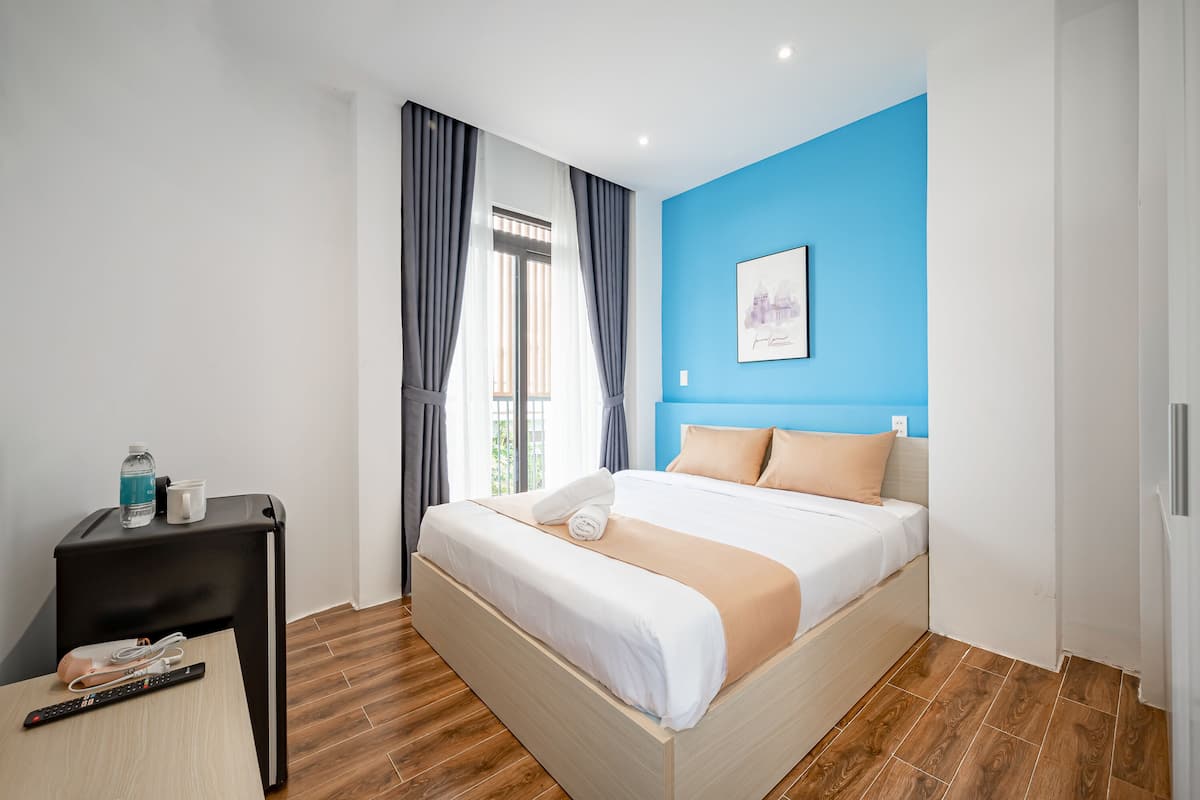 A modern hotel room with a large bed, a small side table with a remote control, and a window with curtains.