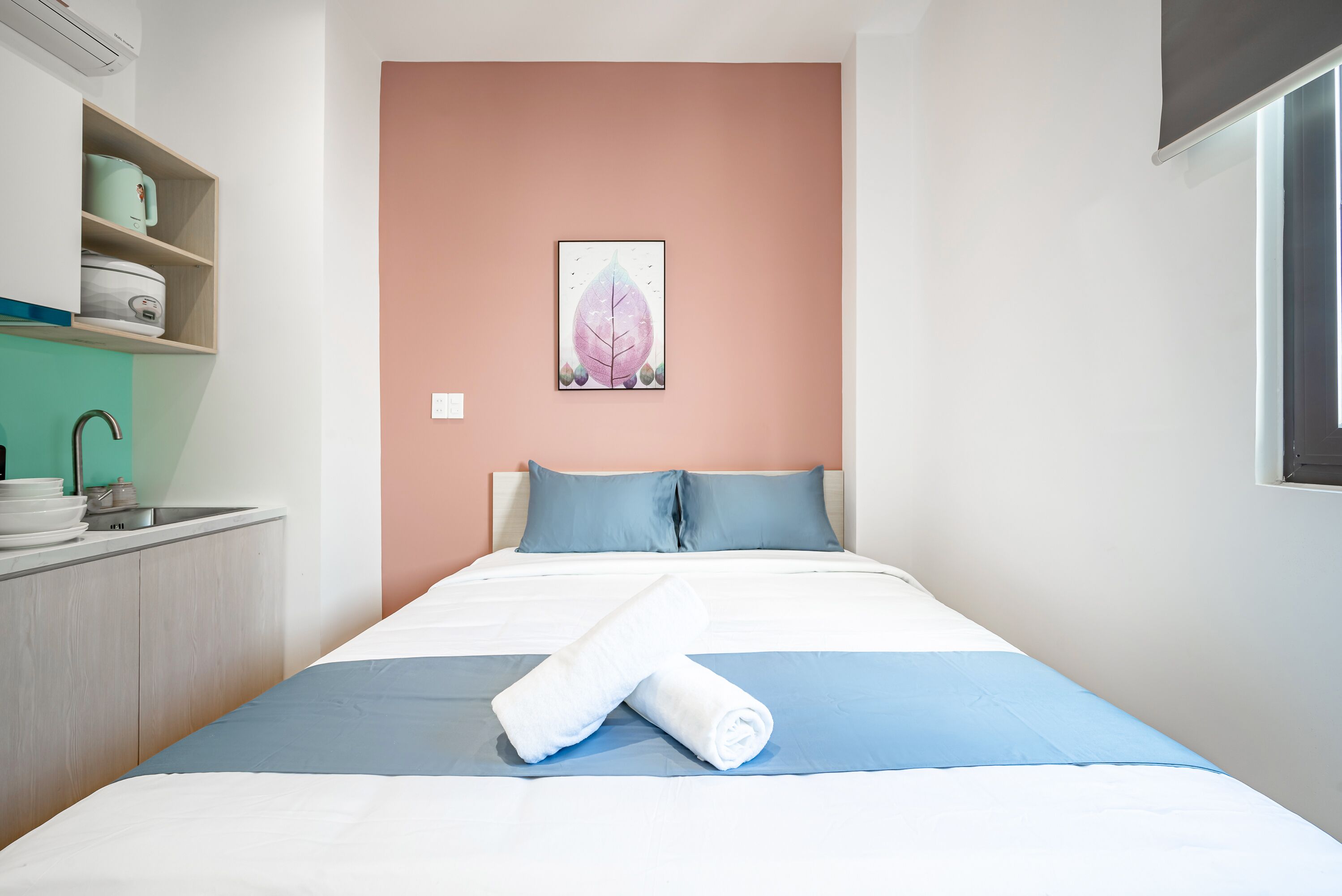 A neatly made bed with a blue and white bedspread, a rolled white towel, and a single pillow.