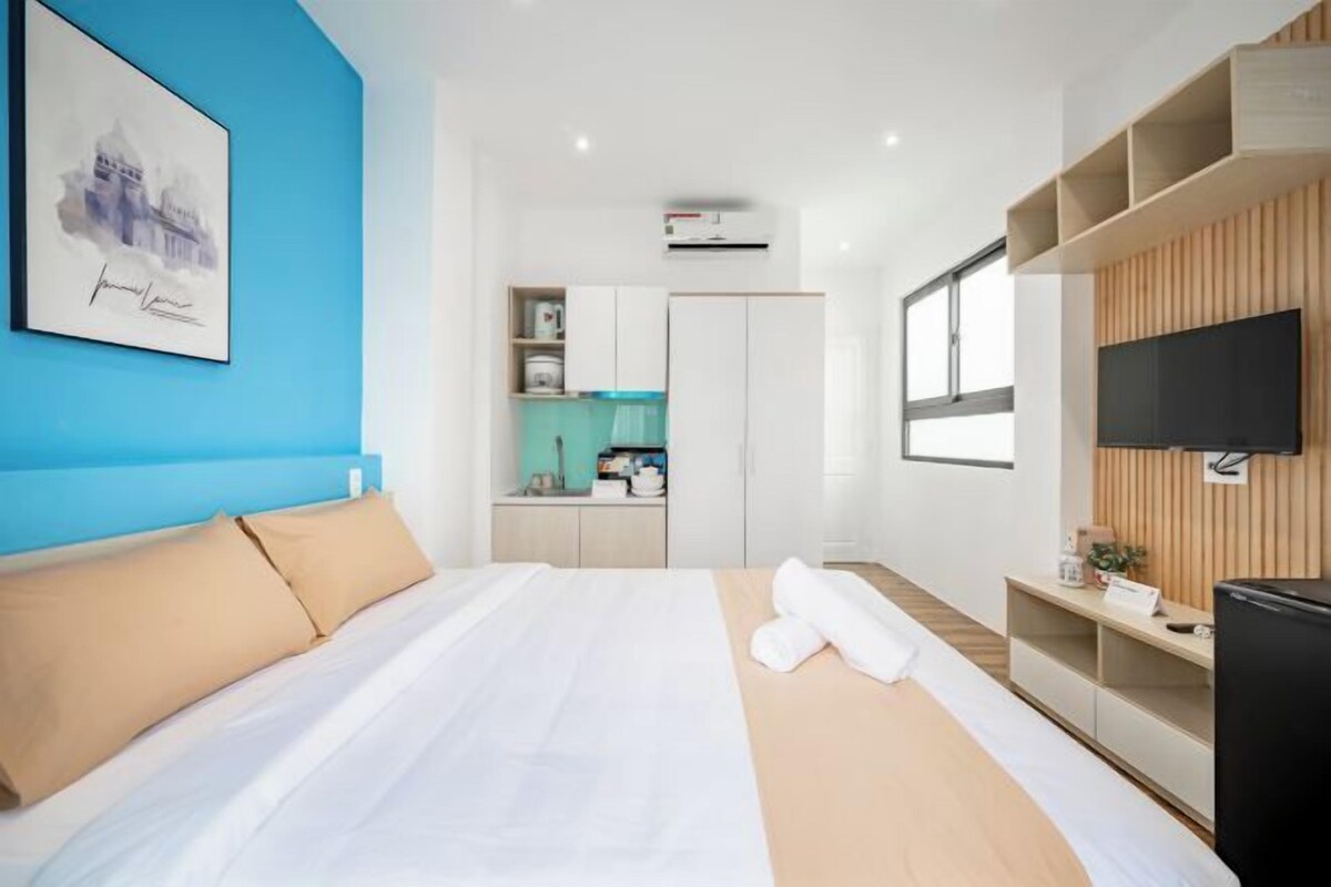 A modern hotel room with a large bed, a TV, a kitchenette, and a blue accent wall.