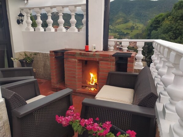 A cozy outdoor seating area with wicker furniture, a brick fireplace, and a view of the countryside. - Cozy 2-BR Apt with mountain view (Antioquia)