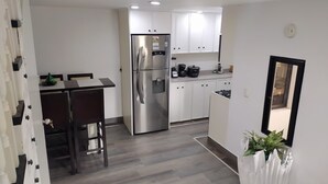 Una cocina moderna con gabinetes blancos, un refrigerador de acero inoxidable, una estufa a gas y un comedor con mesa y sillas de madera oscura.