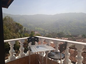 A balcony with a table and chairs, overlooking a hilly landscape with buildings in the distance. - Cozy 2-BR Apt with mountain view (Antioquia)