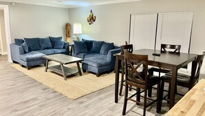 A living room with a sectional sofa, a coffee table, a dining table with chairs, a lamp, and a wall-mounted butterfly decoration. - Spring 12% Discount-April May: The Hidden Jim River Cottage -4 Kayaks (Spring Hill)