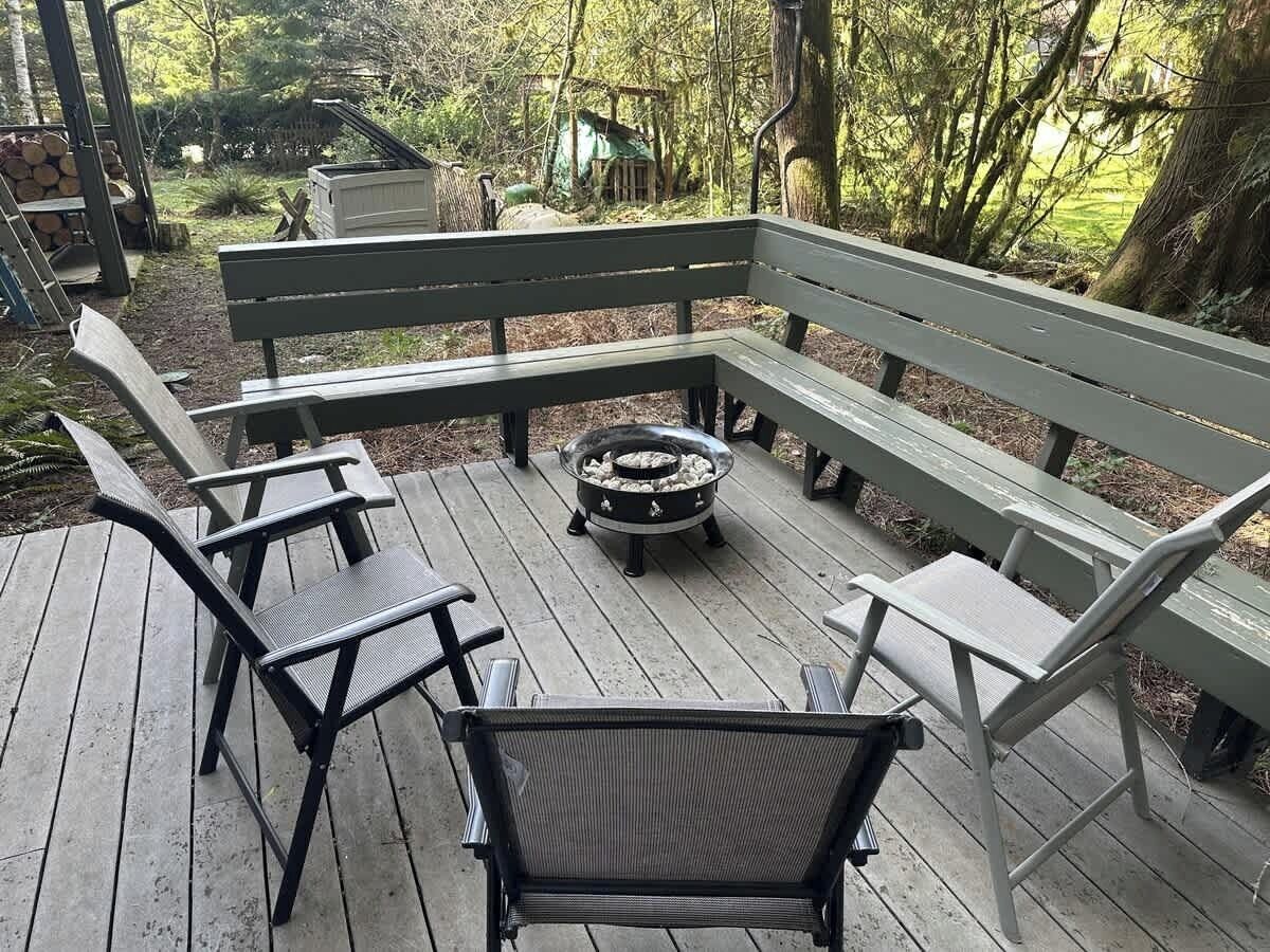 A wooden deck with a fire pit, benches, and chairs.
