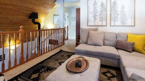 A living room with a wooden staircase, a sofa set, and framed wall art.