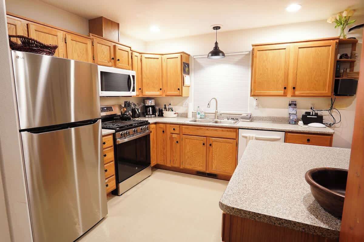 Una cocina con armarios de madera, un refrigerador de acero inoxidable, un microondas, una estufa y un fregadero.