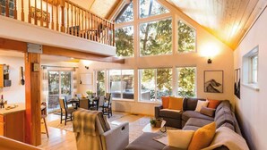 A spacious living area with a large window, a dining area, and a staircase leading to an upper level.