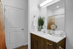 Un baño con una puerta blanca, un lavabo blanco, un espejo y dos jarrones verdes con plantas.
