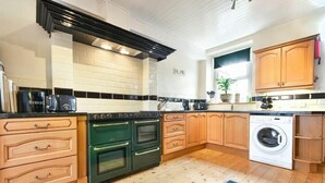 Eine Küche mit Holzausstattung, einer schwarzen Dunstabzugshaube, einem Kombidoppelbackofen, einer Waschmaschine und einer gefliesten Spritzschutzwand.