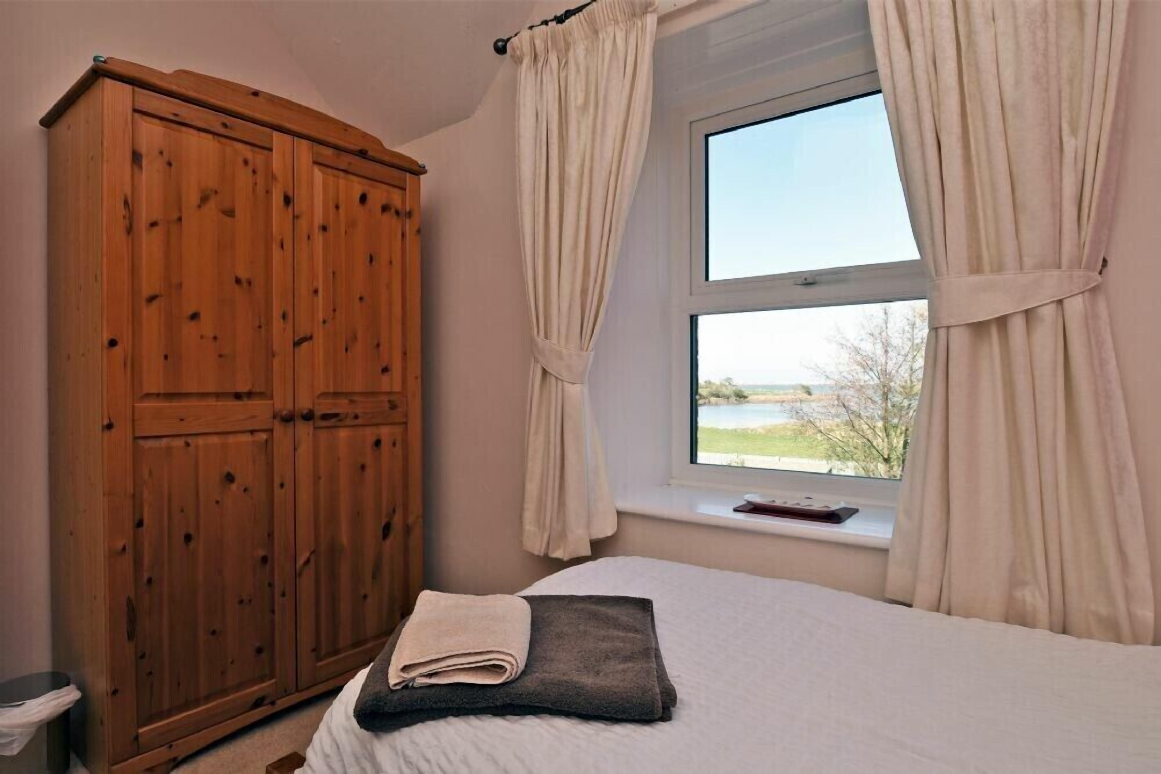 Een slaapkamer met een grote houten garderobe, een bed met een opgevouwen handdoek en een raam met gordijnen.