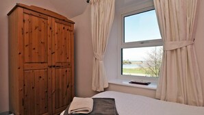 Ein Schlafzimmer mit großem Holzschrank, einem Bett mit gefaltetem Handtuch und einem Fenster mit Vorhängen.