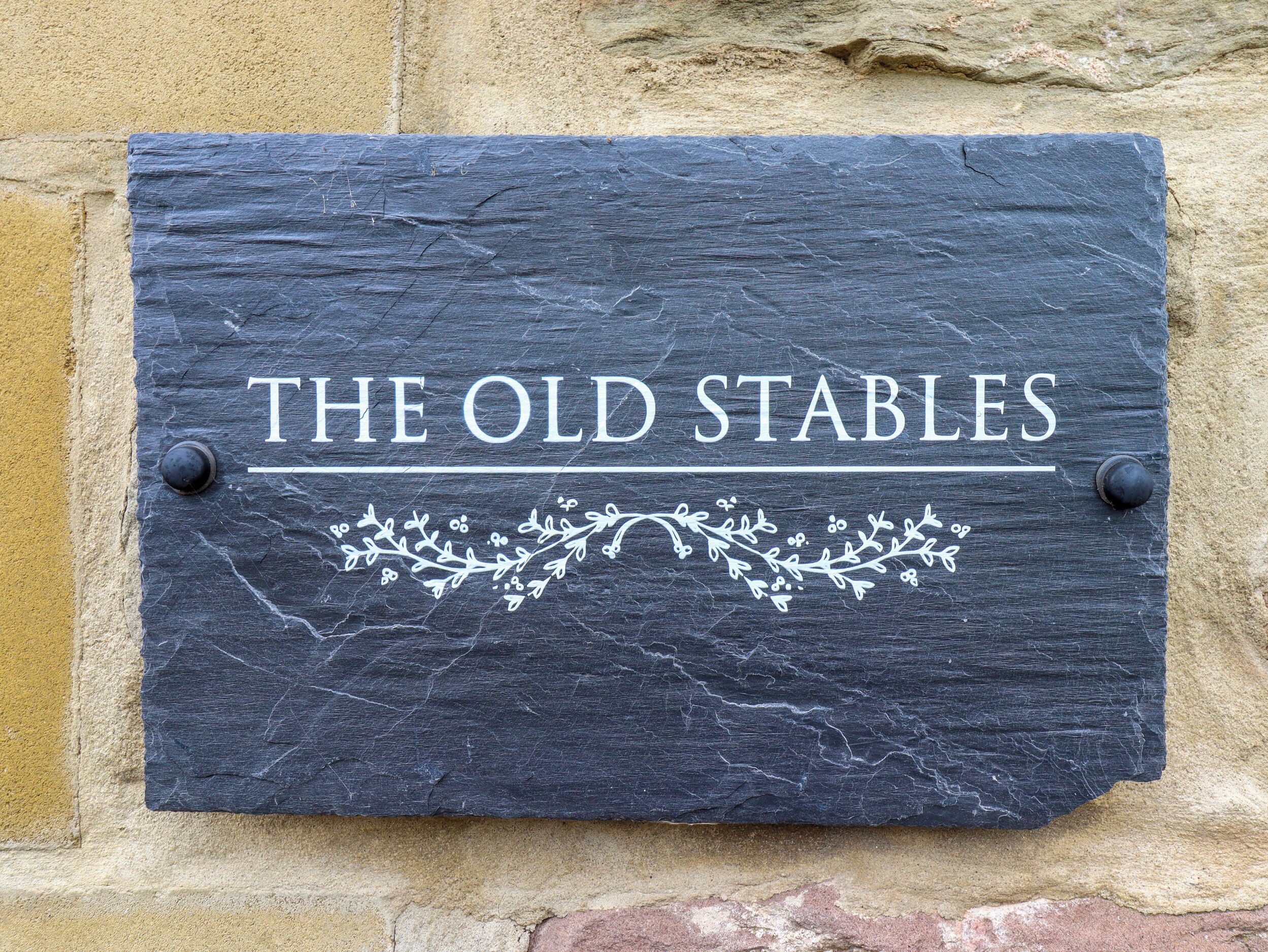 A slate sign with "THE OLD STABLES" written on it, mounted on a textured wall.