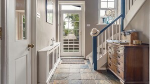 A hallway with a stone floor, a white door, a blue staircase, and a wooden dresser with drawers. - Westhill House (Morpeth)