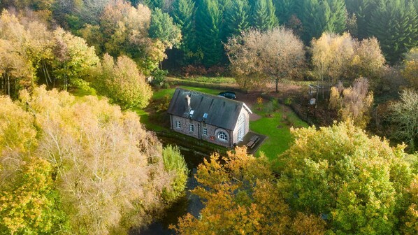 An aerial view of a house surrounded by dense trees and a small pond.