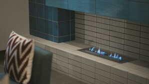 Una chimenea moderna con televisor integrado, paredes con azulejos y un cojín estampado en una silla.