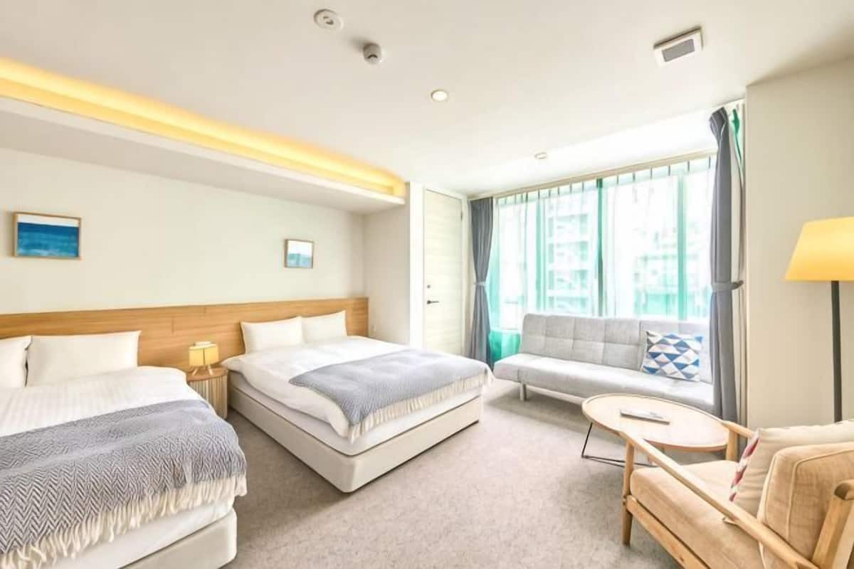 Habitación de hotel con dos camas, un sofá, una mesita y vista a la ciudad.
