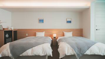 A hotel room with two beds, a wooden headboard, a nightstand with a lamp, and a small shelf with toiletries.