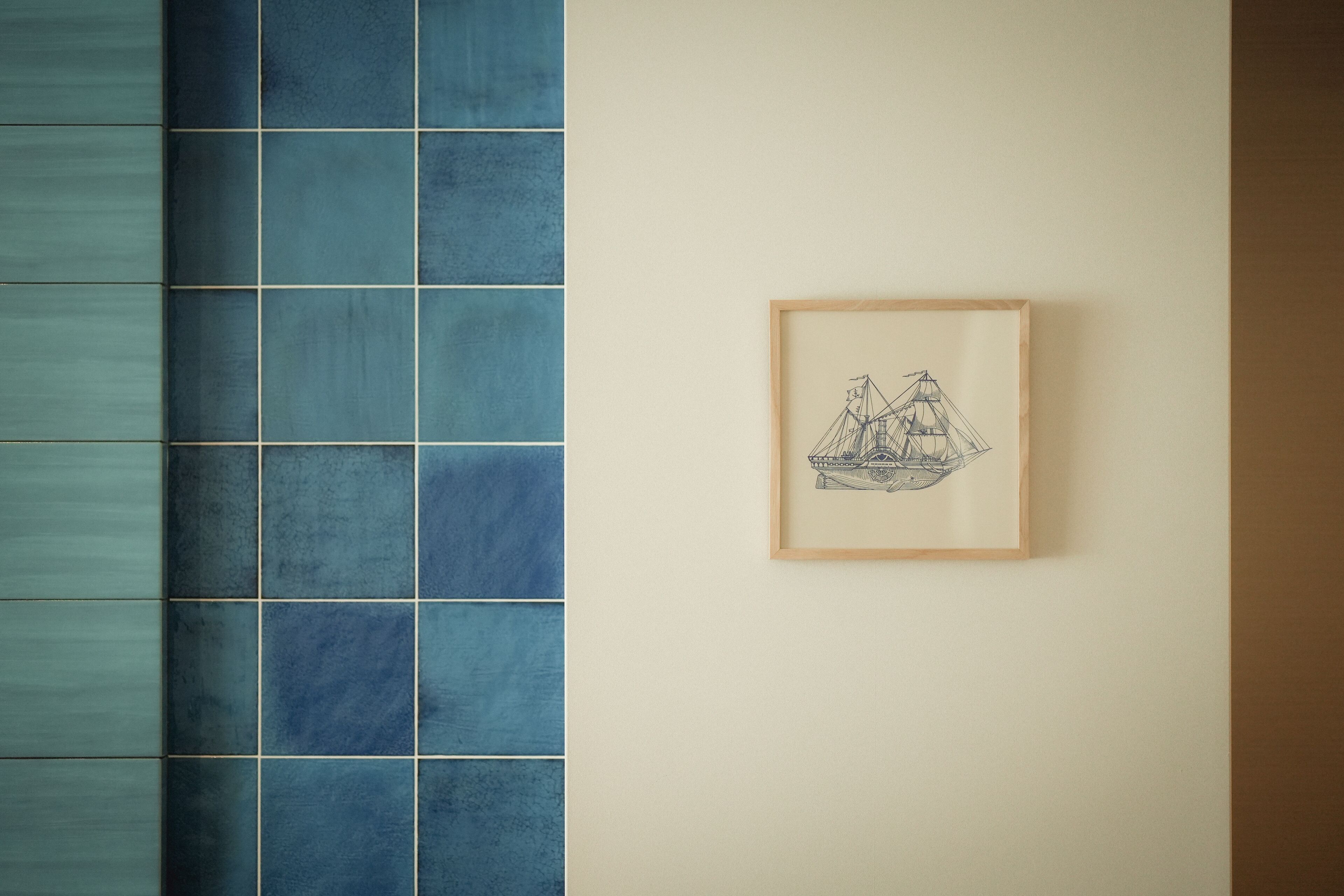 A tiled wall with a framed drawing of a ship.