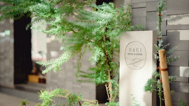 Un letrero para NagI Hotel & Lounge con un diseño minimalista, sobre un fondo de pared de piedra.