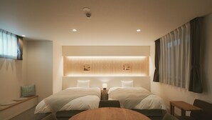 Una habitación de hotel moderna con dos camas, una mesa de madera y una pequeña zona de estar.