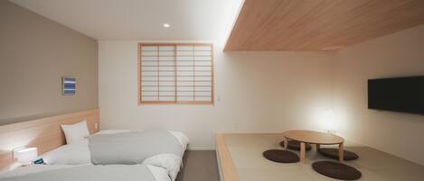 A hotel room with a bed, bedside table, and a small table with cushions.