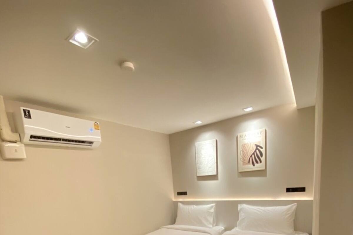 A modern hotel room with two single beds, a built-in air conditioning unit, and a wooden platform.