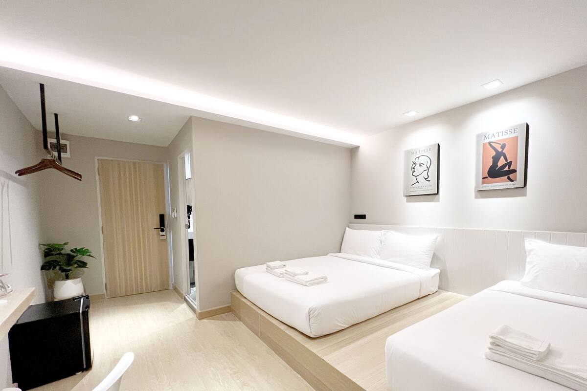 A modern hotel room with a large bed, a smaller bed, a desk, and a hanging coat rack.