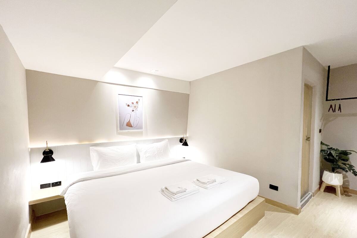 A modern bedroom with a large bed, bedside tables, a wall-mounted light, and a framed picture.