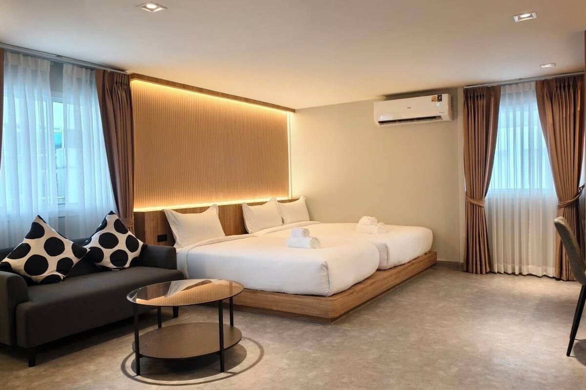 A modern hotel room with a large bed, a sofa, a small round table, and a wooden side table.