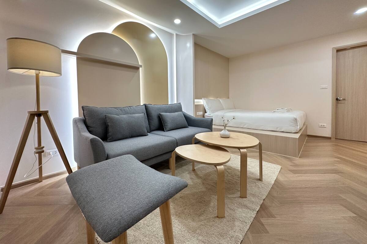 A modern, well-lit room with a sofa, a small table, a lamp, and a bed.
