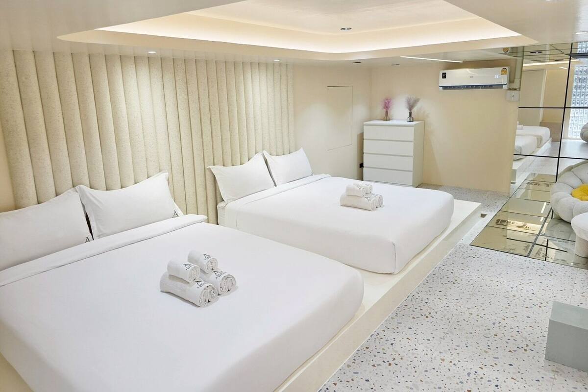 A modern hotel room with two beds, a white dresser, and a small seating area.