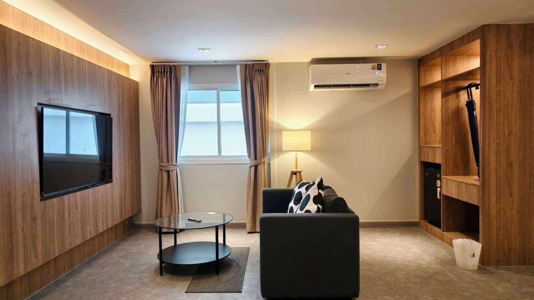 A modern living room with a flat-screen TV, a round coffee table, a sofa, a lamp, and built-in wooden shelving.
