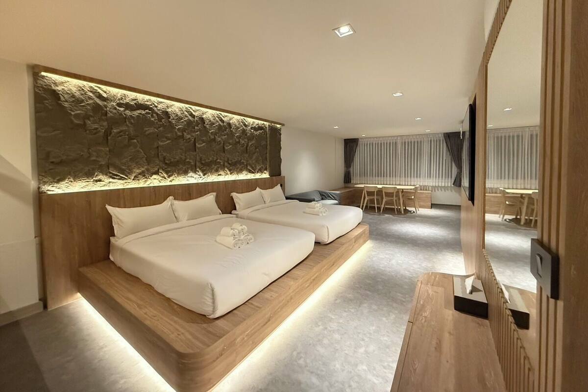 A modern hotel room with two beds, a dining area, and a large mirror.