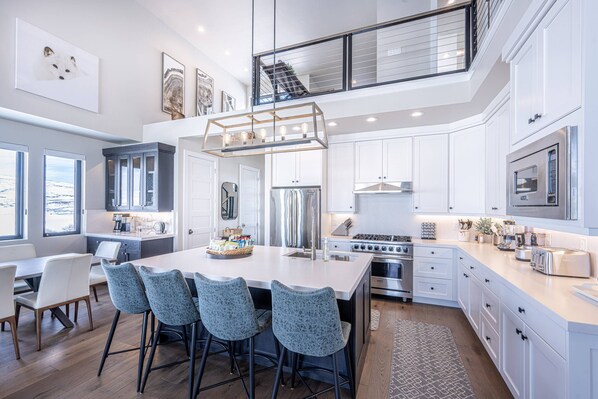 A modern kitchen with a large island, stainless steel appliances, and a high ceiling with a balcony.