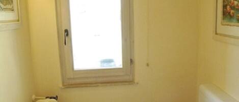 A small bathroom with a toilet, a radiator, a window, and a toilet paper holder.