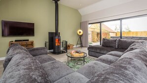 Una sala de estar moderna con chimenea, sofás grises grandes, un televisor de pantalla plana y un ventanal amplio.